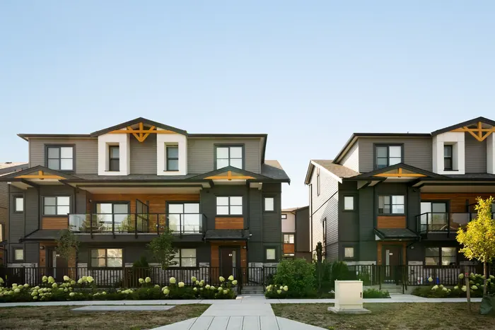 Photograph of two three-storey Elwynn Green townhome buildings from the street, with gabled roofs, wood accents, balconies and a landscaped path between them