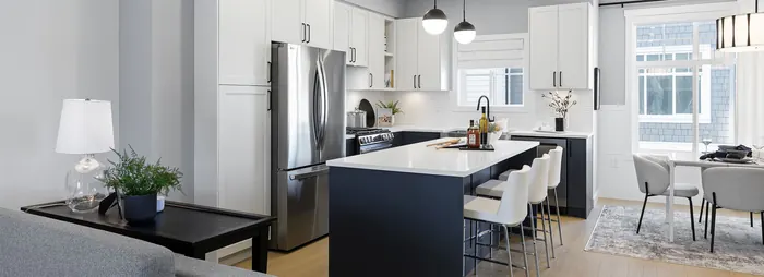 Photograph of a kitchen with white cabinets, a dark island with stools and a dining area by the windows