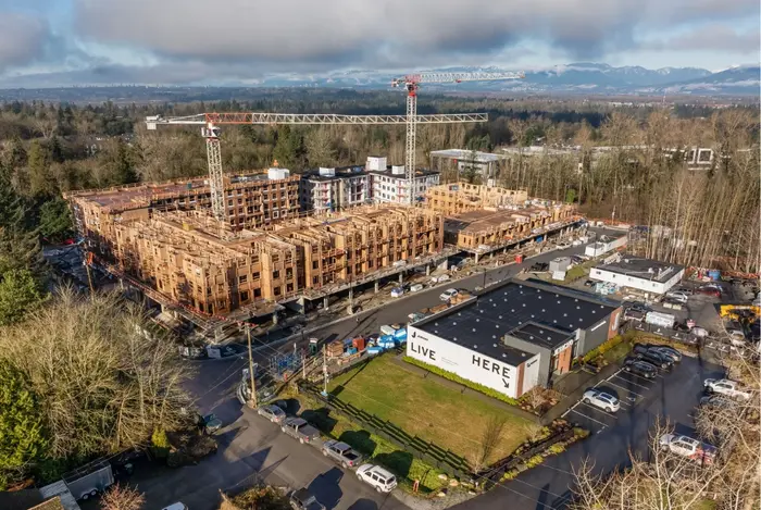 Aerial photograph of Jericho Park under construction: a large six-storey wood-framed building near completion with a tower crane beside it, and a Live Here billboard on the lot across the road