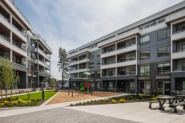 Photograph of a courtyard between Park & Maven condo buildings with lawn, paving, a playground and picnic tables