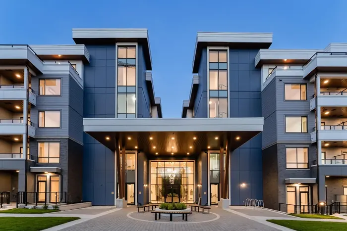 Photograph of the lit entrance of a Park & Maven condo building at dusk, a blue five-storey building with a glass lobby