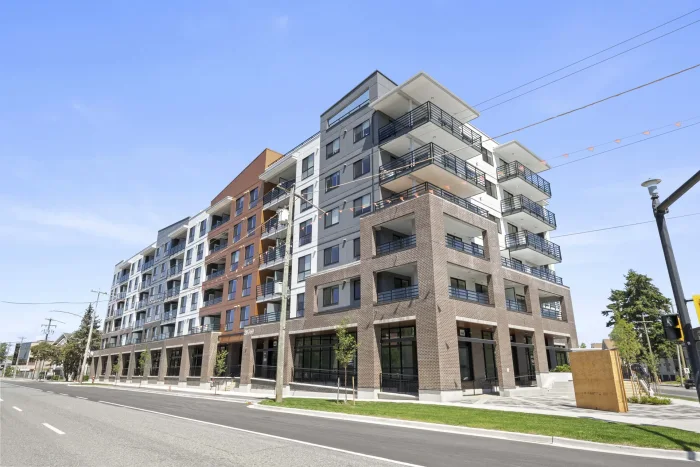 Artist’s rendering of Unity South Langley from Fraser Highway: a six-storey condo building in earthy tones with a glazed commercial frontage at street level and a landscaped plaza with seating